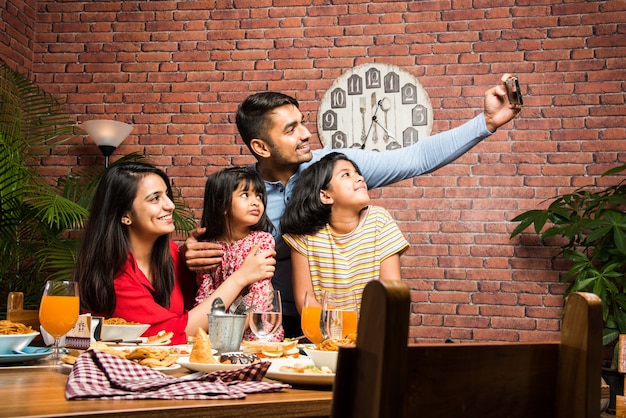 Indische junge vierköpfige Familie Essen am Esstisch zu Hause oder im Restaurant. Südasiatische Mutter, Vater und zwei Töchter beim gemeinsamen Essen