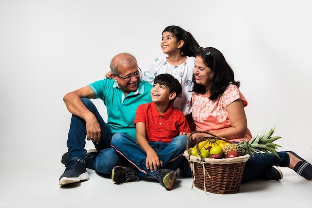 Indische Kinder mit Großeltern, die lächeln, während sie auf einem weißen Hintergrund drinnen sitzen, selektiver Fokus