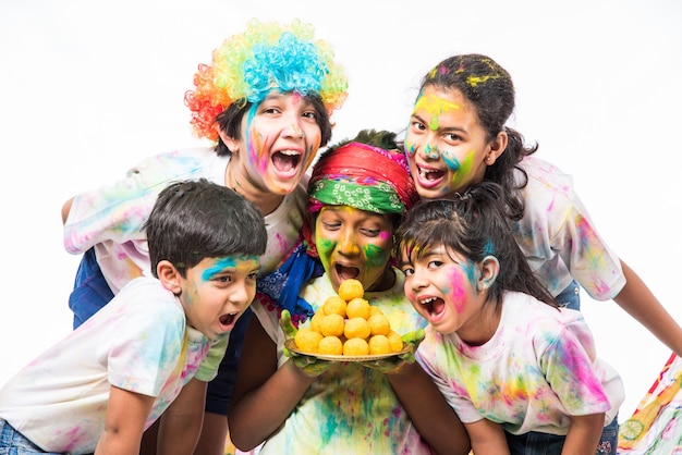 Indische kleine Kinder oder Freunde oder Geschwister, die das Holi-Fest mit Gulal- oder Pulverfarbe, Süßigkeiten, Pichkari oder Spray feiern, einzeln auf weißem Hintergrund