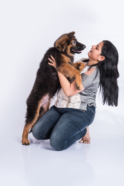 Indische oder asiatische junge Dame, die mit einem Schäferhundwelpen spielt, isoliert auf weißem Hintergrund