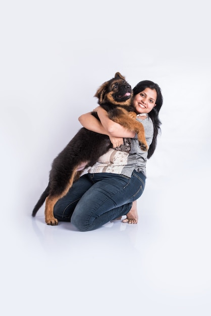 Indische oder asiatische junge Dame, die mit einem Schäferhundwelpen spielt, isoliert auf weißem Hintergrund