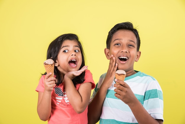 Indische oder asiatische süße kleine Kinder, die Eiscreme oder Mangoriegel oder Süßigkeiten essen. Auf buntem Hintergrund isoliert