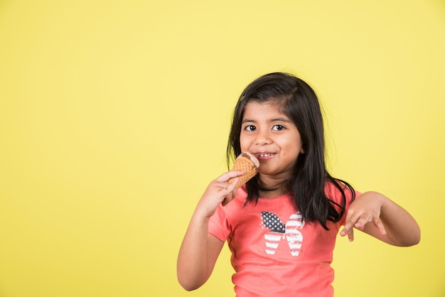 Indische oder asiatische süße kleine Kinder, die Eiscreme oder Mangoriegel oder Süßigkeiten essen. Auf buntem Hintergrund isoliert