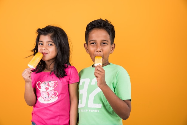 Indische oder asiatische süße kleine Kinder, die Eiscreme oder Mangoriegel oder Süßigkeiten essen. Auf buntem Hintergrund isoliert