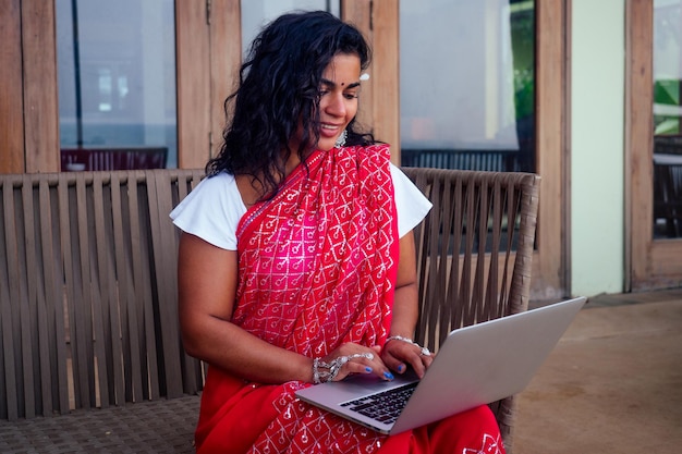 Indische schöne Geschäftsfrau, die an einem modernen Laptop im Café-Restaurant am Ufer des Paradiesozeans arbeitet. Web Designer-Mädchen-Freiberuflerin in Indien im Meer. Fernarbeit, Konzepttexter