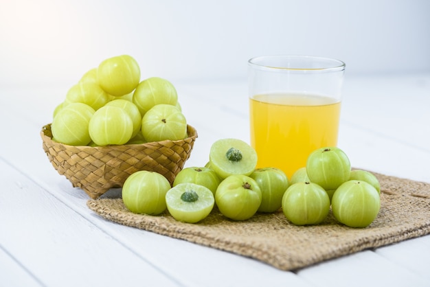 Indische Stachelbeere im Weidenkorb und im Saft, Sackcloth auf weißem Holztisch