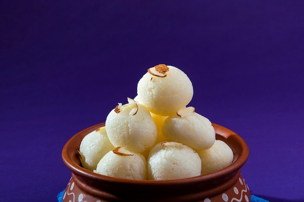 Indische Süßigkeit oder Nachspeise - Rasgulla, Berühmte bengalische Süßigkeit in Tonschale mit blauer Serviette auf violettem Hintergrund