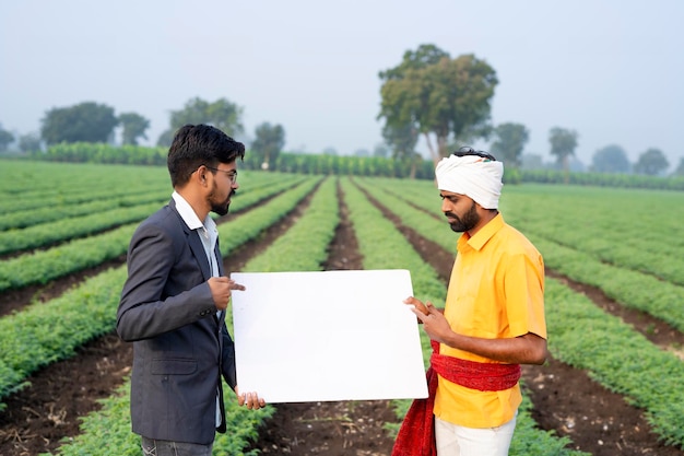 Indischer Agronom oder Offizier mit Bauer auf dem Landwirtschaftsfeld mit Whiteboard