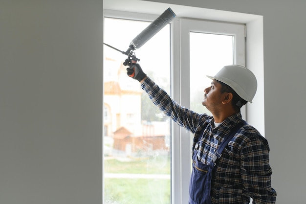 Indischer Arbeiter verwendet einen Silikonschlauch zur Reparatur eines Fensters im Innenbereich