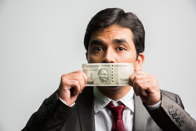 Indischer asiatischer Geschäftsmann, der Geldschein für Mund oder Gesicht hält
