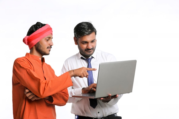 Indischer Bankbeamter oder Angestellter der Unternehmensregierung, der dem Landwirt im Laptop einige Informationen zeigt.