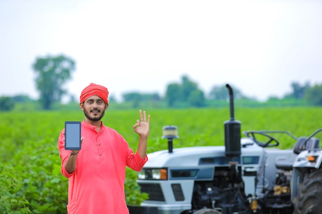 Indischer Bauer, der einen mobilen Bildschirm am Landwirtschaftsfeld zeigt