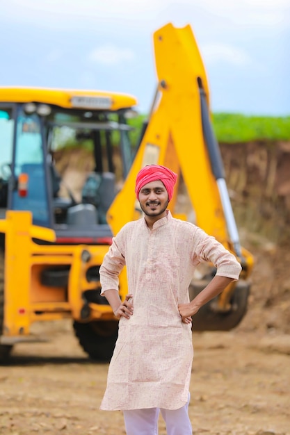 Indischer Bauer, der mit seiner neuen Erdbewegungsmaschine steht.