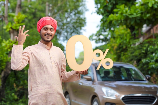 Indischer Bauer, der Null-Prozent-Schild hält und mit neuem Auto steht