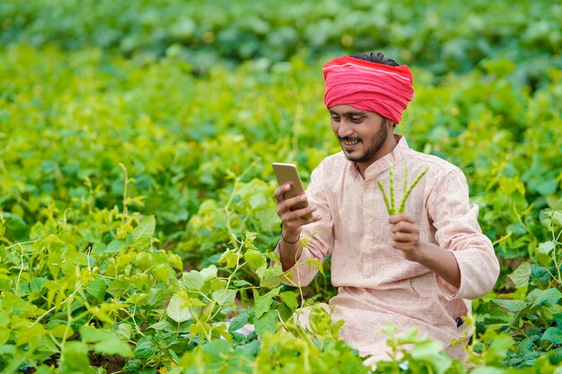 Indischer Bauer, der Smartphone am Landwirtschaftsfeld verwendet.