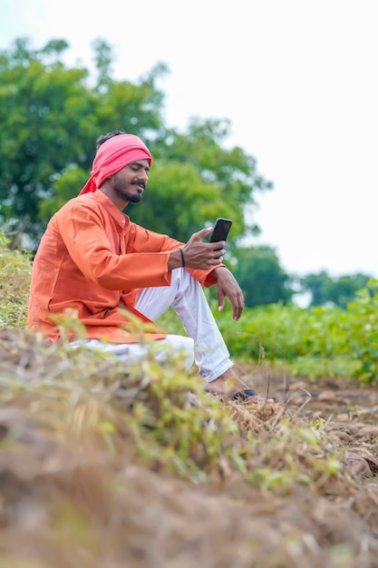 Indischer Bauer, der Smartphone auf dem Landwirtschaftsgebiet verwendet