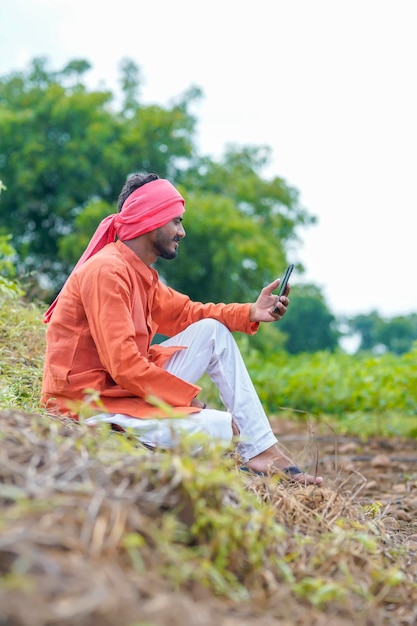 Indischer Bauer, der Smartphone auf dem Landwirtschaftsgebiet verwendet