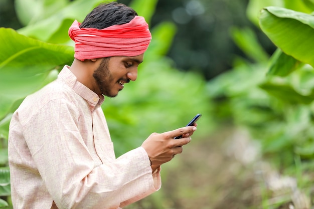 Indischer Bauer, der Smartphone im Bananenlandwirtschaftsfeld verwendet.