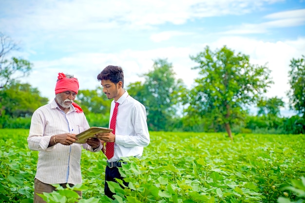 Indischer Bauer mit Agronom am Baumwollfeld und Agronom, der einige Informationen auf Briefblock schreibt