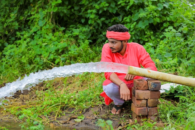 Indischer bauer mit wasserfluss vom rohr am feld