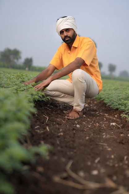 Indischer Bauer sitzt auf dem Landwirtschaftsfeld oder zeigt Finger