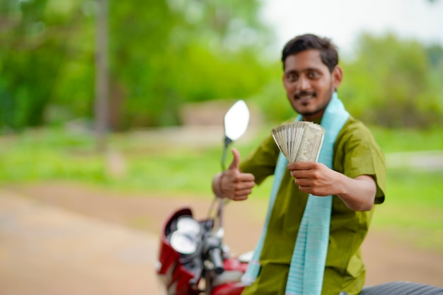 Indischer Bauer sitzt auf seinem neuen Fahrrad und zeigt Geld.