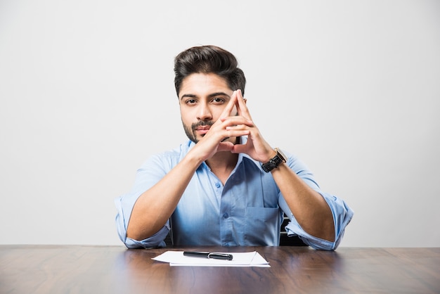 Indischer Geschäftsmann, der ein Dokument schreibt, während er am Schreibtisch oder Arbeitsplatz sitzt