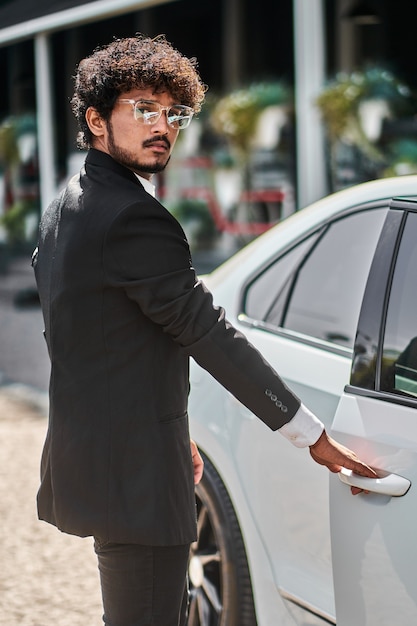Indischer Geschäftsmann öffnet Tür im weißen Auto.