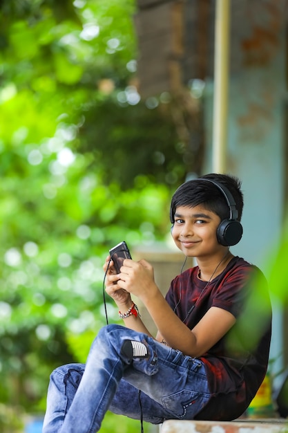 Indischer Junge, der Musik hört oder auf Handy lernt