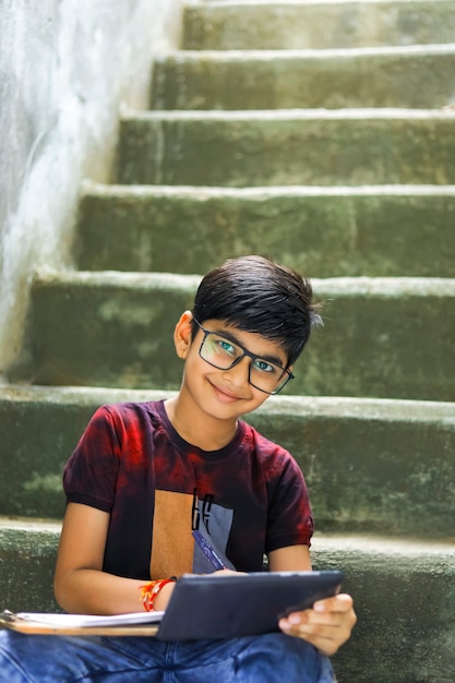 Indischer kleiner Junge, der online mit Handy zu Hause studiert