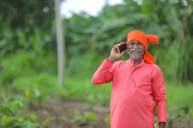 Indischer Landwirt, der auf Handy am Landwirtschaftsfeld spricht