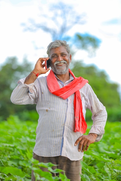 Indischer Landwirt, der Handy am Landwirtschaftsfeld spricht