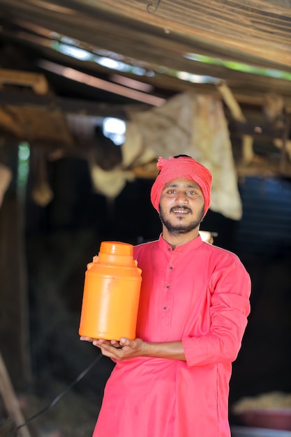 Indischer Landwirt, der Milchflasche in der Hand auf Milchfarm hält