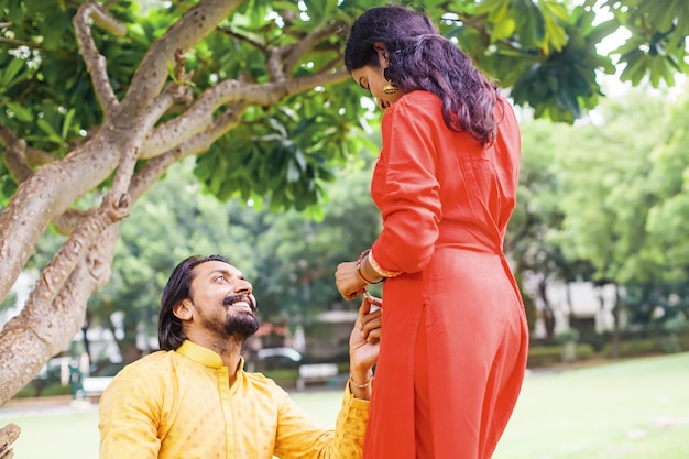 Indischer Mann kniet nieder, um seiner Freundin im Garten einen Heiratsantrag zu machen