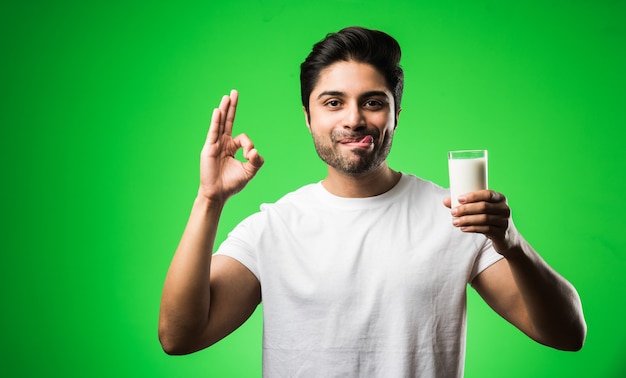 Indischer Mann trinkt Milch im Glas, während er isoliert steht