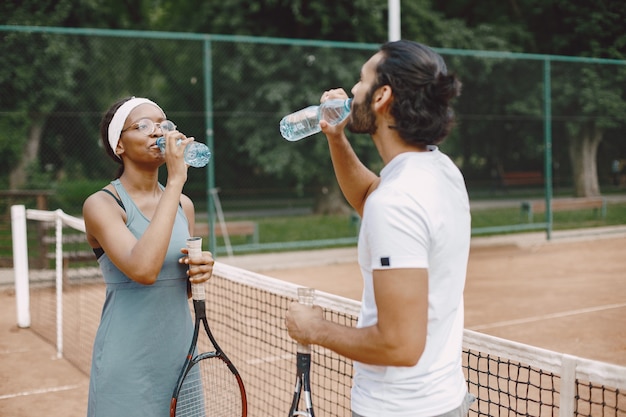 Indischer Mann und schwarze Amerikanerin stehen auf einem Tennisplatz