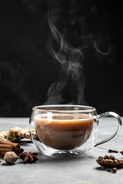 Indischer Masala-Chai-Tee Heißer Masala-Chai-Gewürztee mit Milch und Gewürzen wird in ein Glasglas auf dunklem Hintergrund gegossen, vertikaler Bildplatz für Text