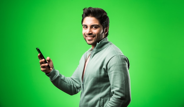 Indischer oder asiatischer Mann mit Smartphone, der das Mobiltelefon benutzt, während er isoliert steht