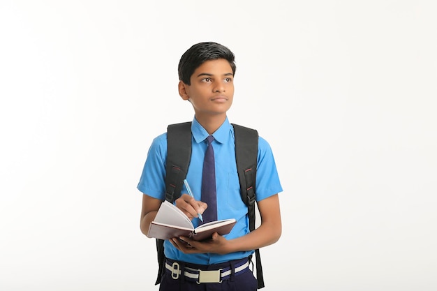 Indischer Schuljunge in Uniform und mit Tagebuch in der Hand auf weißem Hintergrund