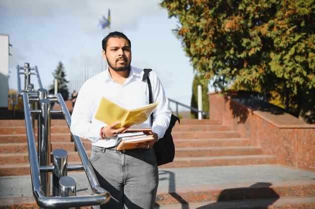Indischer Student mit Rucksack, der Bücher am sonnigen Tag hält