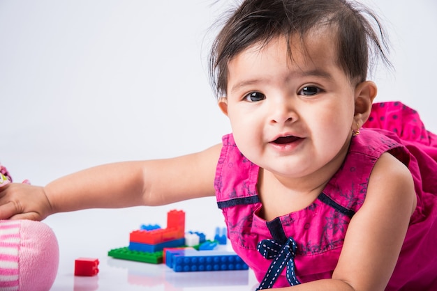 Indisches Baby, das mit Spielzeug oder Blöcken spielt, asiatisches Kleinkind, das mit Spielzeug auf weißem Hintergrund spielt, indisches Baby, das mit Spielzeug spielt, indisches Kleinkind, das mit Spielzeug spielt, während es auf dem Boden liegt