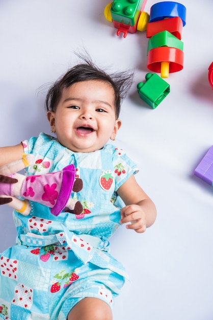 Indisches Baby, das mit Spielzeug oder Blöcken spielt, asiatisches Kleinkind, das mit Spielzeug auf weißem Hintergrund spielt, indisches Baby, das mit Spielzeug spielt, indisches Kleinkind, das mit Spielzeug spielt, während es auf dem Boden liegt