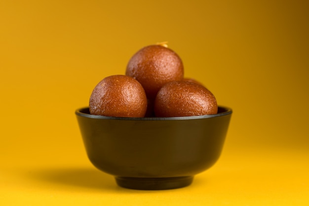 Indisches Dessert oder süßes Gericht: Gulab Jamun in der Schüssel auf gelbem Hintergrund.