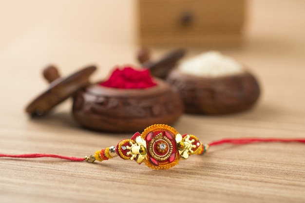 Indisches Festival: Raksha Bandhan Hintergrund mit einem eleganten Rakhi, Reiskörner und Kumkum