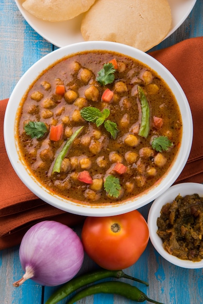 Indisches Gericht würziges Kichererbsen-Curry, auch bekannt als Chola oder Chana Masala oder allgemein Chole, serviert mit gebratenem Puri oder Poori auf buntem oder hölzernem Hintergrund. Selektiver Fokus