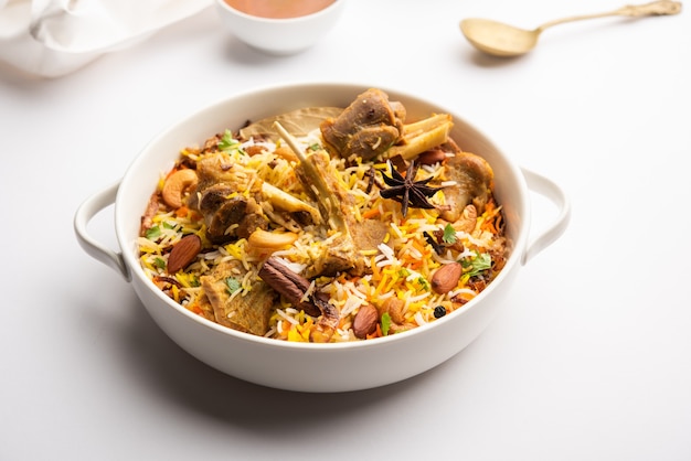 Indisches Hammel-Biryani, zubereitet in Basmati-Reis, serviert mit Joghurt-Dip über stimmungsvollem Hintergrund, Selektiver Fokus