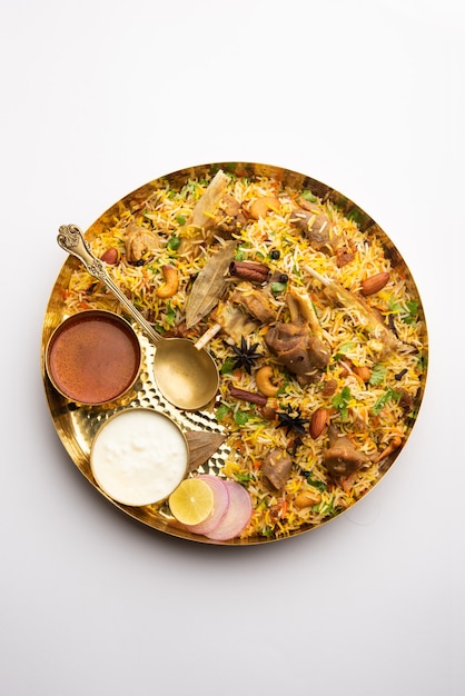 Indisches Hammel-Biryani, zubereitet in Basmati-Reis, serviert mit Joghurt-Dip über stimmungsvollem Hintergrund, Selektiver Fokus