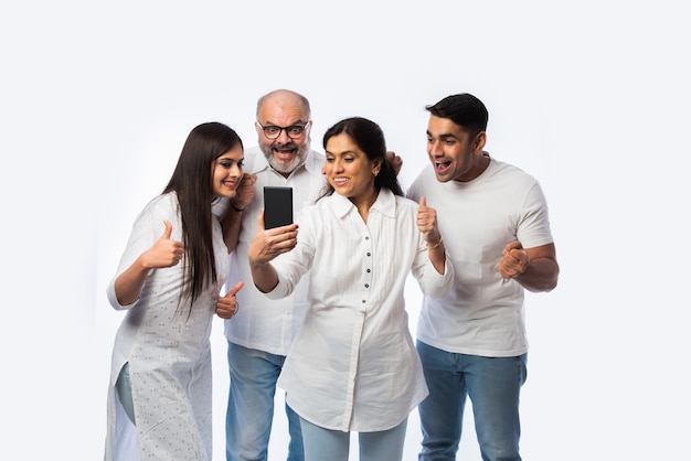 Indisches junges Paar mit Eltern, die Smartphone mit glücklichen Ausdrücken verwenden oder halten, gegen Weiß stehend