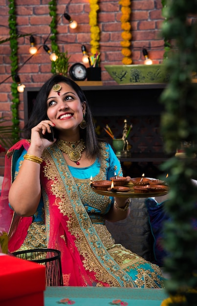 Indisches Mädchen, das Diwali Diya in traditioneller Kleidung hält, auf ein Selfie-Bild klickt oder über das Smartphone spricht.