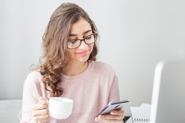 Indisches Mädchen, das einen Handy und einen Tasse Kaffee hält.